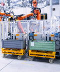 Industrial setting with robotic arms and heavy duty steel casters on carts for efficient material handling.