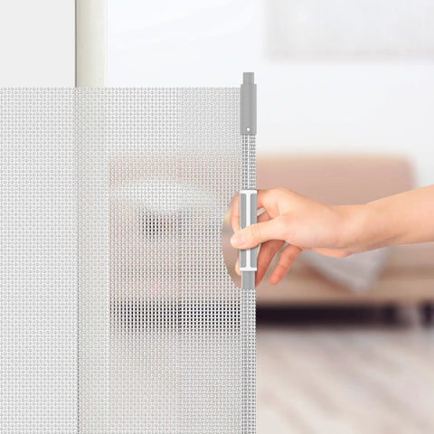 Hand operating a gray retractable baby and pet safety gate, 54 inch wide, 34 inch tall, for doorways and stairs, indoor and outdoor use.