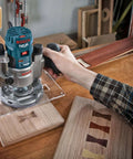 Bosch router (teal) being used on wood; part of RBS015MBS 15-piece carbide-tipped router bit set.