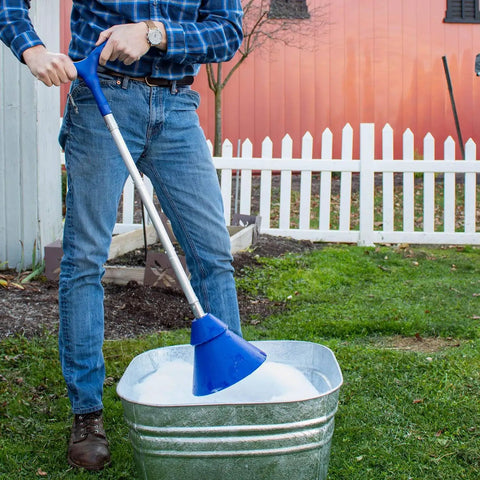 Person using a Portable Manual Clothes Washer Plunger with blue head in a bucket for laundry in outdoor setting.