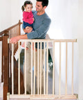 Parent holding child next to Walk-Through Top Of Stairs Baby Gate In Natural Wood With Four Point Mount, One Hand Release, Dual-Direction Swing