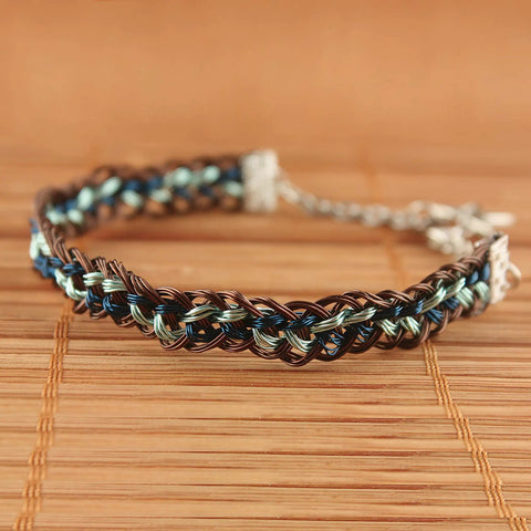 Close-up of a braided bracelet with brown, blue, and green threads woven using a round kumihimo disk for jewelry making.