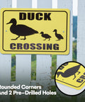 Reflective Duck Crossing sign on fence with black silhouette of ducks, yellow background, and rounded corners for outdoor safety.