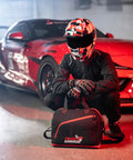 Racer with helmet near car, holding Fleece Lined Motorcycle And Racing Helmet Bag With Hidden Shoe Compartment Waterproof 600D Oxford Gear Carrier.