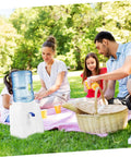 Family enjoying a picnic with Portable Desktop Water Dispenser For Camping, Office And Home, compact water cooler visible on blanket.
