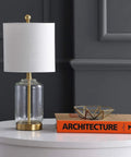 Brass gold and clear glass table lamp with white linen drum shade on white table, glam transitional bedside light for living room.