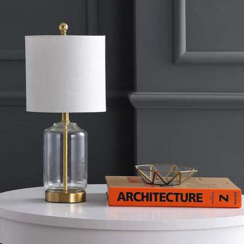 Brass gold and clear glass table lamp with white linen drum shade on white table, glam transitional bedside light for living room.