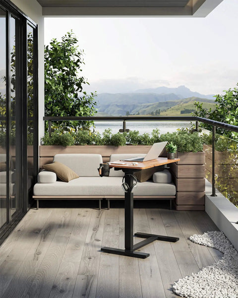 Yihayo Electric Height Adjustable Overbed Table W/ Wheels, 24x16 Inch mobile nursing stand desk by a balcony with laptop.