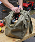 Tough As Nails Waxed Canvas Military Duffle Bag With Water Resistance, Adjustable Strap, Heavy Duty Zippers, Fully Lined Interior, And Built In Tool Organizer For Contractors And DIYers on a workbench.