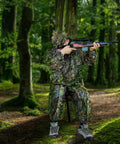 Person using Camo Tree Hammock Chair Portable Hunting Stool for outdoors with camouflage suit, tree attachment, in a forest setting.