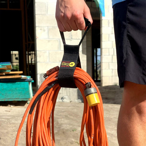 Person holding Wrap-It Storage Straps 17-Inch 2-Pack Heavy-Duty Hook And Loop Cord Carrier with orange extension cord