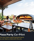 Koda 16 Natural Gas Pizza Oven for Outdoor Cooking, showing a pizza baking on the black durable steel body, with people dining.