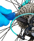 Blue gloved hand using Drivetrain Clean Brush With Contoured Tip Designed To Wipe Grit From Tight Crannies And Reach Every Corner Of Your Bike Chain And Cassette Dual Sided Cleaning Tool In Blue GSC 3 For Quick Pro Level Bike Maintenance on rear cassette