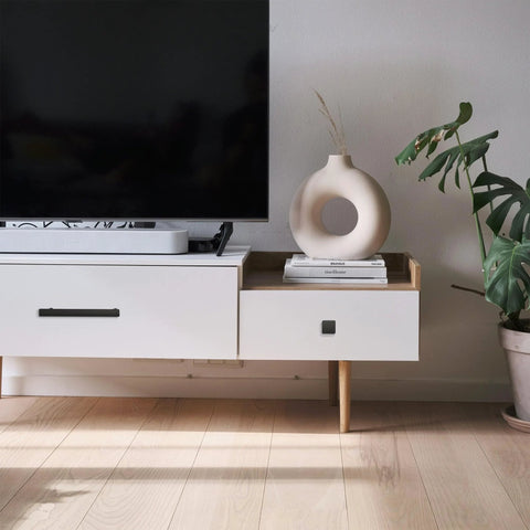 White modern console table with decorative vase and books next to a large TV, featuring sleek lines and minimalist decor style.