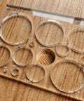 A Damn Sharp Transparent Acrylic Router Template For Woodworking Boasts Thirteen Circle Sizes Packed In A Single Piece on wood surface.