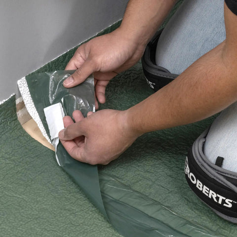Person installing Real Deal 3 In 1 Flooring Underlayment Roll For Laminate And Engineered Wood against a wall.