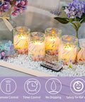 Flameless Real Wax Floral LED Candles With Remote And Timer 4 Pack For Home Decor Parties And Holiday Tables Glass Covered Flickering Candles Create Cozy Ambience Without Mess placed on white stones with flowers and remote control.