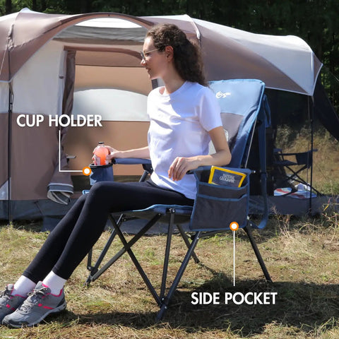 Woman sitting on oversized folding high back lawn chair for adults with cup holder, carrying strap, hard armrests, 400Lb capacity, blue.