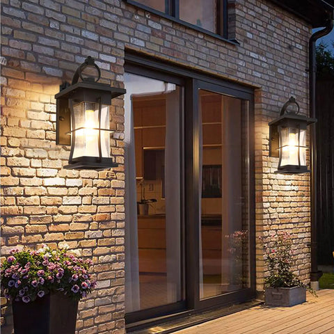 Dusk To Dawn Outdoor Wall Lantern With Sensor, Matte Black Porch Light illuminating a brick patio with plants.