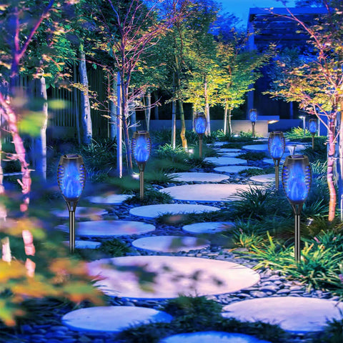 Blue Outdoor Solar Torch Lights 12 Pack With Flickering Flame Waterproof Mini Tiki Torches installed along a garden pathway.