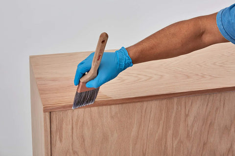 Person applying Water Based Pre Stain Wood Conditioner For Even Stain, 1 Quart, Clear Finish on wooden surface with brush