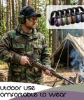 Man wearing 12 Pack Adults And Kids Ear Protection Earmuffs With 27 Db Noise Reduction in a forest, with tent and campfire nearby.
