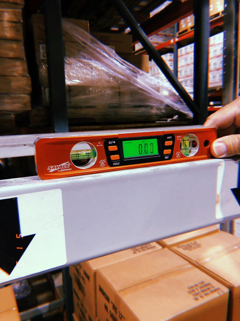 Savage Digital Magnetic Torpedo Level, 9 Inch Aluminum Billet, Orange, Displaying 0 Degrees on Metal Shelf, Warehouse Setting