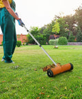 Person using Roller Thatch Rake For Lawn With 15 Inch Dethatcher And Smooth Rolling Wheels No Fuss Easy Glide Adjustable 0 To 15 Degrees Extendable 38 To 68 Inch Handle Heavy Duty Metal Yard Care Tool For Dead Grass And Thatch Cleanup on grass.