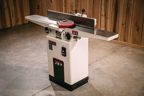 Six Inch Long Bed Jointer Featuring Helical Cutterhead And 27 Carbide Inserts Gives Dead Nuts Precision And Glassy Smooth Results Paired With Versatile Dual Voltage Hookup For That Sweet Shop Upgrade You Want, showing machine with cast iron base and steel tables.
