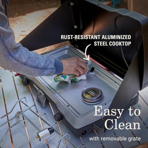 Cleaning the Two-Burner Propane Camp Stove With InstaStart Ignition And Wind Guards, showcasing rust-resistant cooktop.