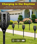 6 solar tiki torches with realistic flickering flames installed in a garden, featuring 4 Pack 96 LED Solar Tiki Torches With Flickering Flame 43 Inch Tall Outdoor Lights Waterproof For Garden Patio Yard Pathway Halloween Decor Easy Setup Durable Night Lighting That Delivers Realistic Fire Look And Cozy Vibe