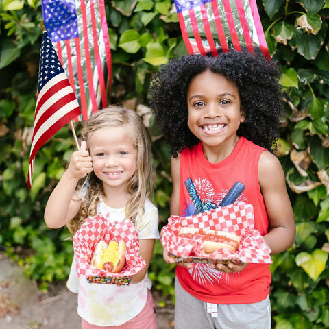 Children holding hot dogs and 12 Pack 8x12 Inch American Flags on Sticks for Outdoor Use at a backyard event.