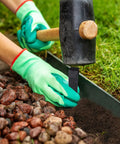 Inserting 30 Pack 10 Inch Garden Landscape Stakes for lawn edging with mallet and gloves, next to grass and mulch.
