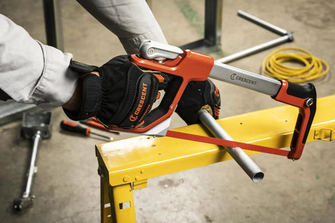 12 Inch Fast Tension Hacksaw With Dual Material Handle, sawing metal pipe on yellow workbench, ergonomic front grip visible