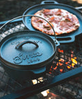 Pre Seasoned 2 Qt Cast Iron Dutch Oven With Flat Bottom For Stovetop And Campfire Use next to a grilled pizza on campfire