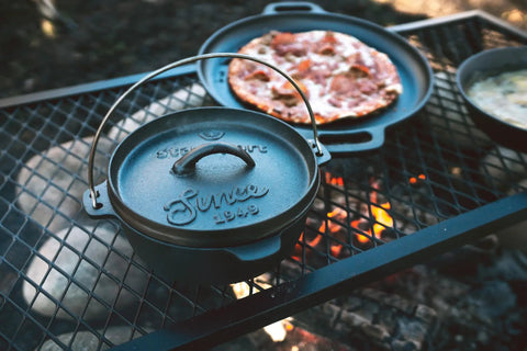 Pre Seasoned 2 Qt Cast Iron Dutch Oven With Flat Bottom For Stovetop And Campfire Use next to a grilled pizza on campfire