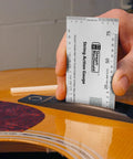 Hand using String Action Gauge And Ruler In Inches Stainless Steel For Gearheads Lifetime Durability Swiss Army Style Tech Tool With Pinpoint String Height Nut Height Saddle Slot Depth And Pickup Polepiece Height on acoustic guitar