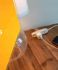 Slimline Flat Plug Extension Cord 6 Foot 16 Gauge 3 Conductor 3 Outlet Indoor White Wall Saver on wooden table with devices