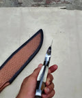 Hand holding Stag Handle Fixed Blade Knife For Camping And Hunting, showing handle detail with leather sheath beside it.