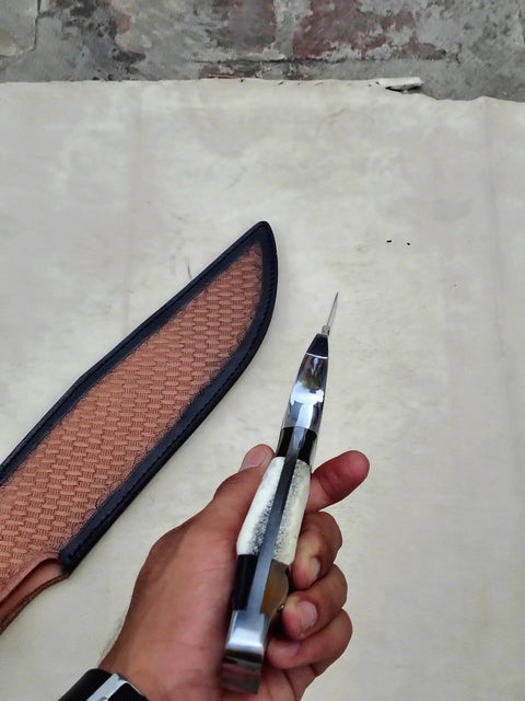 Hand holding Stag Handle Fixed Blade Knife For Camping And Hunting, showing handle detail with leather sheath beside it.