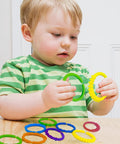 Child holding 24 Colorful Teething Ring Links For Babies Plastic Chain Toy Set For Strollers, multiple colors visible on table