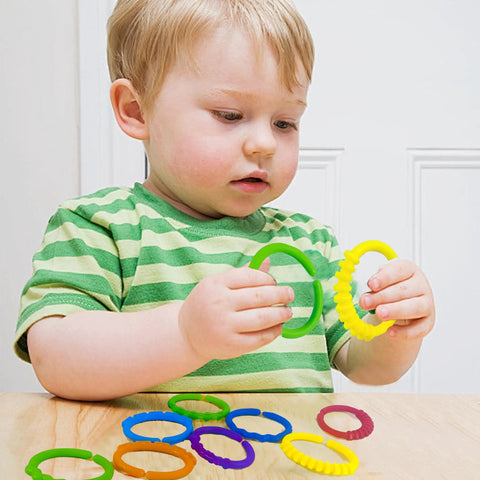 Child holding 24 Colorful Teething Ring Links For Babies Plastic Chain Toy Set For Strollers, multiple colors visible on table