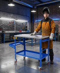 Heavy Duty Steel Welding Table And Portable Workbench Featuring Adjustable Height Three Tilt Angles And Locking Casters For Serious Shop Builds And Grinds in a workshop with a welder standing by.