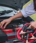 Person using jumper cables from Roadside Emergency Car Kit With 30 Piece Road Trip Essentials Tool Set Including Jumper Cables, Tire Pressure Gauge, Gloves, Electrical Tape, And Carrying Case For Car, Truck, Or RV Gray Red.