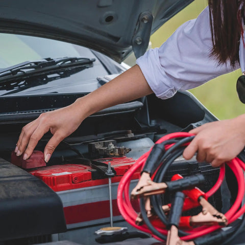 Person using jumper cables from Roadside Emergency Car Kit With 30 Piece Road Trip Essentials Tool Set Including Jumper Cables, Tire Pressure Gauge, Gloves, Electrical Tape, And Carrying Case For Car, Truck, Or RV Gray Red.