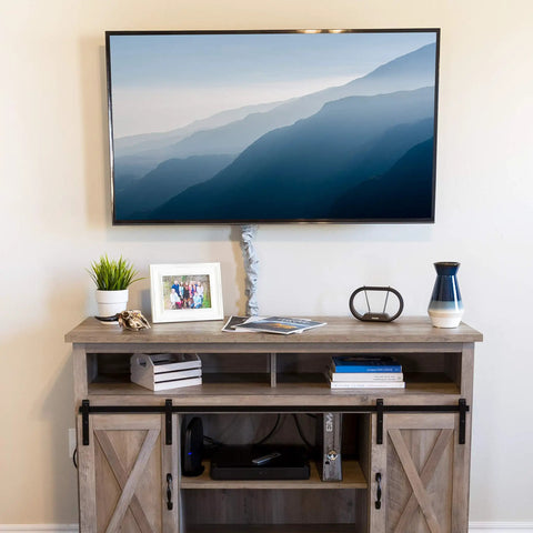 Living room with TV mounted above a wooden cabinet, featuring decor items like books, framed photo, and plant pot.