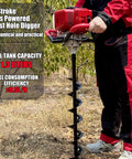 Man using Beast Of A 52cc Gas Powered Post Hole Digger Earth Auger with red handles and spiral bit on grassy terrain.