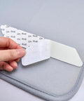 Close-up of a hand peeling a sticky corner of an 8 Pack Washable Non Slip Rug Pads Double Sided For Floors Black Reusable Rug Grips