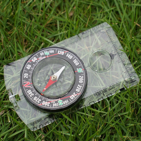 Outdoor Compass Kit With Adjustable Declination, Magnifier, Ruler And Scale laying on grass, transparent design, close-up view