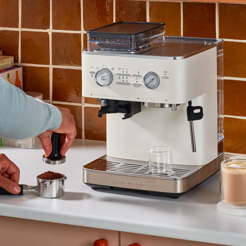 Semi Automatic Espresso Machine With Built In Burr Grinder And Smart Dosing Tech For Smooth One Or Two Shot Pulls Sturdy Metal Body In Porcelain White being used to tamp coffee.